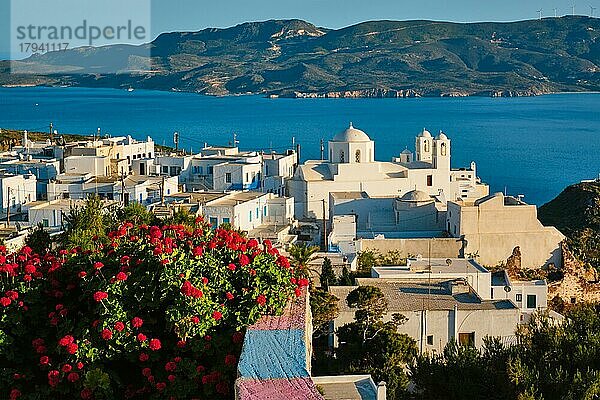 Malerischer Blick auf die griechische Stadt Plaka auf der Insel Milos über rote Geranienblüten. Plaka Dorf  Milos Insel  Griechenland. Fokus auf Blumen