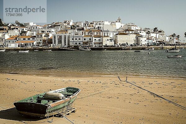 Stadtbild einer weiß getünchten Stadt mit einem traditionellen hölzernen Fischerboot am Strand im Vordergrund  Ferragudo  Algarve  Portugal  Europa