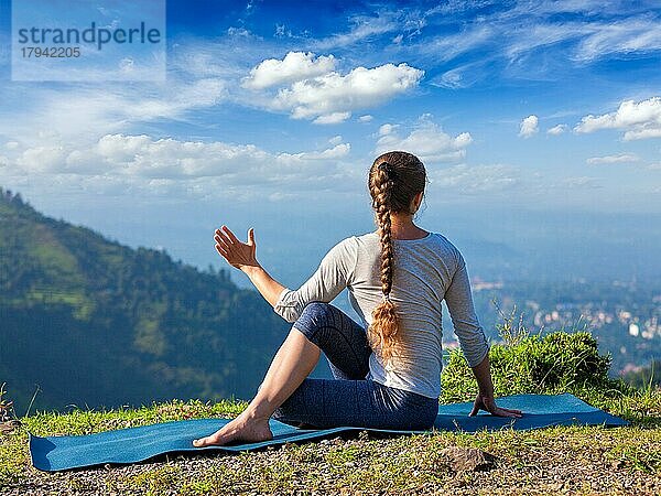 Hatha Yoga im Freien  sportlich fitte Frau bei der Yoga-Asana Parivrtta Marichyasana (oder Ardha Matsyendrasana)  sitzende Wirbelsäulendrehung im Freien in den Bergen am Morgen