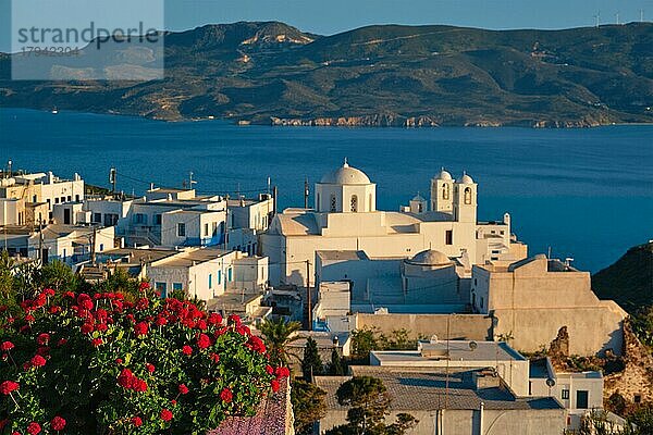 Blick auf das Dorf Plaka auf der Insel Milos über rote Geranienblüten bei Sonnenuntergang. Plaka Stadt  Insel Milos  Griechenland. Fokus auf Blumen