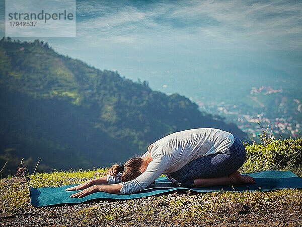 Sportliche  fitte Frau übt Yoga-Asana Balasana  Kind-Pose im Freien in den Bergen. Vintage Retro-Effekt gefiltert Hipster-Stil Bild