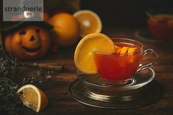 Tee mit Orange in Tasse  auf hölzernen Untergrund  vor Halloweendekoration