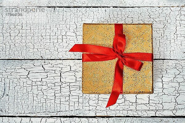 Geschenk Geburtstag Weihnachtsgeschenk Konzept  gelbes Gold Geschenk-Box mit rotem Band auf weiß lackiertem Holz Hintergrund. Ansicht von oben