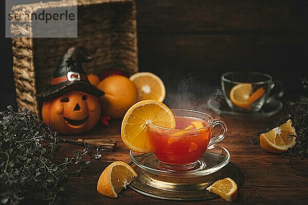 Tee mit Orange in Tasse  auf hölzernen Untergrund  vor Halloweendekoration