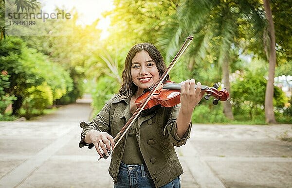 Junge Frau spielt Geige im Freien. Porträt eines Mädchens  das im Freien Geige spielt  Nahaufnahme eines Mädchens mit ihrer Geige  das im Freien eine Melodie spielt  Konzept einer lächelnden Geigerin