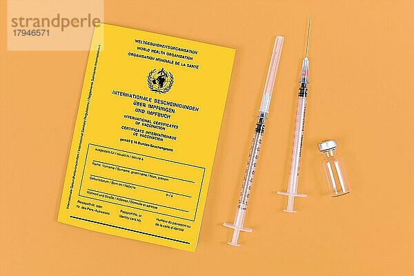 Impfstoffkonzept mit Spritzen  Fläschchen und gelber internationaler Impfbescheinigung auf orangefarbenem Hintergrund