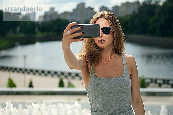 Attraktive Tourist Mädchen macht Selfie mit Flussufer auf Hintergrund in Stadtpark