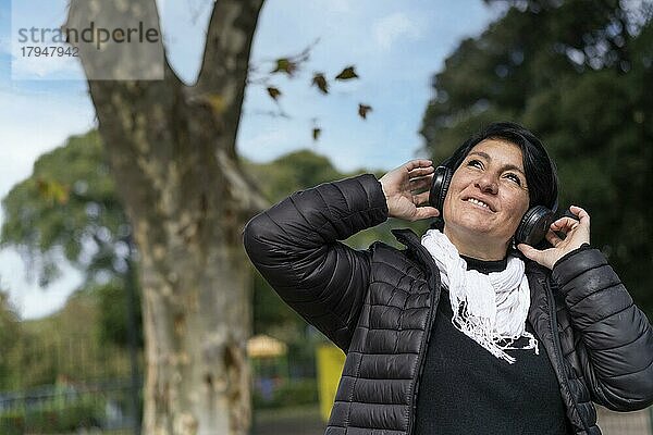 Lateinamerikanische Frau  die im Freien mit Kopfhörern Musik hört. Ausdruck von Glück  gewinnende Haltung. Textfreiraum