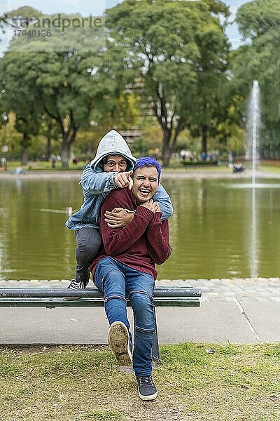 Homosexuelles lateinamerikanisches Paar sitzt auf einer Bank in einem Park und lacht