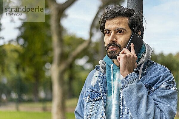 Junger lateinamerikanischer Mann  der in einem Park mit seinem Handy telefoniert