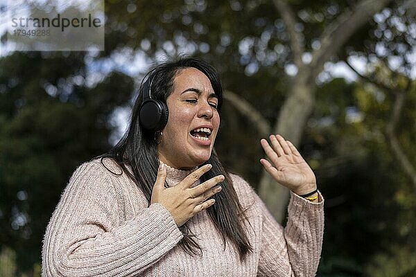 Junge lateinamerikanische Frau  die im Freien mit Kopfhörern Musik hört. Ausdruck von Glück  gewinnende Einstellung. Textfreiraum