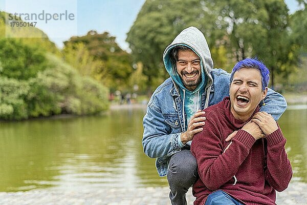 Homosexuelles lateinamerikanisches Paar sitzt auf einer Bank in einem Park und lacht