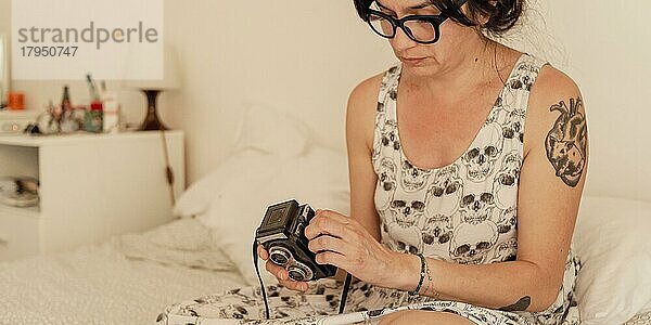 Hispanische junge erwachsene Frau  die eine Pause zu Hause in ihrem Schlafzimmer einlegt und ihre alte analoge Kamera überprüft  ein sonniger Morgen im Sommer