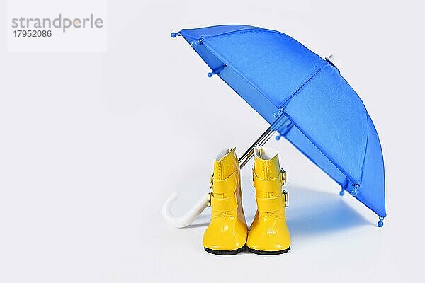 Regenkonzept mit blauem Regenschirm und gelben Gummistiefeln