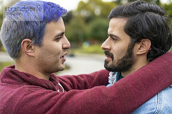Lateinische Homosexuell Paar umarmt in einem Park Blick auf einander über zu küssen