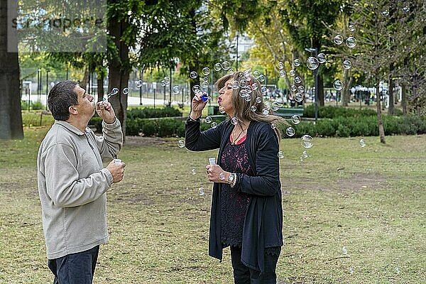Fröhliches reifes queeres Paar bläst Seifenblasen in einem Park