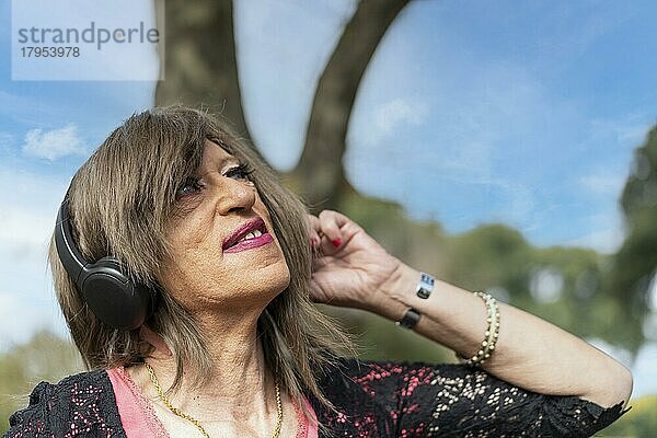 Transfrau hört Musik im Freien mit Kopfhörern. Ausdruck von Glück  gewinnende Haltung. Textfreiraum