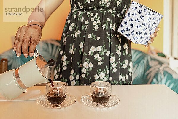 Junge Frau gießt Kaffee in Glastassen in der Küche zu Hause  ein sonniger Morgen im Sommer