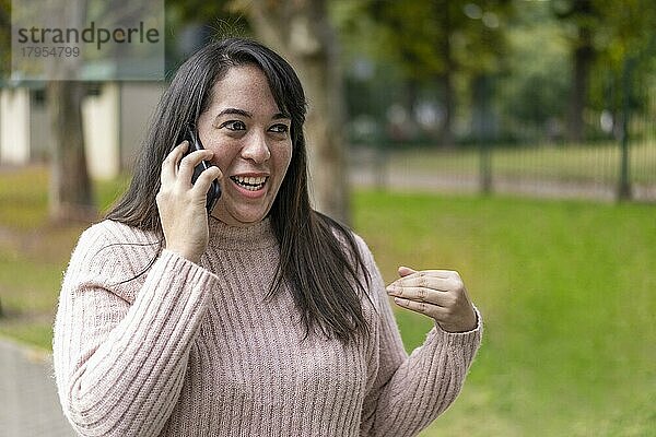 Junge lateinamerikanische Frau  die in einem Park mit einem Handy telefoniert