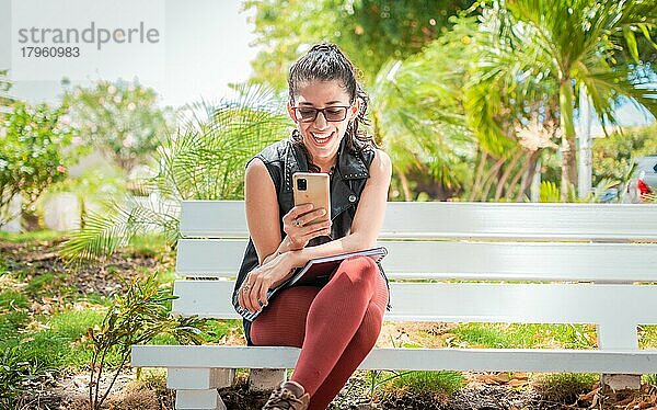 Mädchen sitzt auf einer Bank und überprüft ihr Handy  Glückliche Frau sitzt in einem Park und schreibt eine SMS auf ihrem Handy  Frau sitzt auf einer Bank und sendet eine SMS