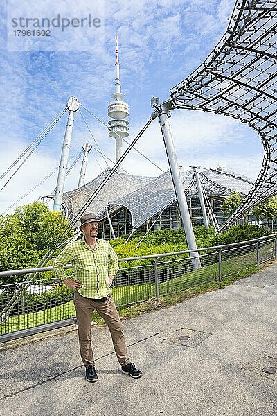 Freundlich lächelnder Mann beim Olympiaturm mit Olympia-Zeltdach  Olympiapark  Olympiagelände  München  Oberbayern  Bayern  Deutschland  Europa