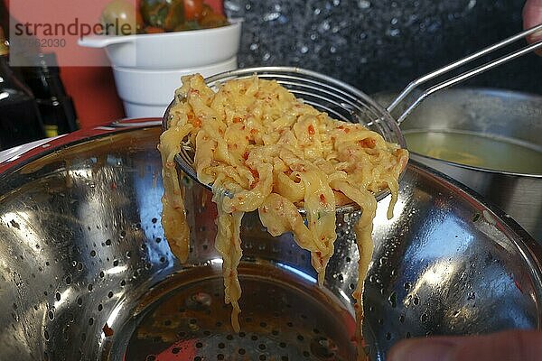 Schwäbische Küche  Zubereitung handgeschabte Spätzle für Spätzle-Auflauf  dreierlei Spätzle  Spätzle mit roter Paprika mit Schaumlöffel aus Kochwasser entnehmen  Mehlspeise  typisch Schwäbisch  Traditionsküche  vegetarisch  Foodfotografie  Studio  Deutschland  Europa