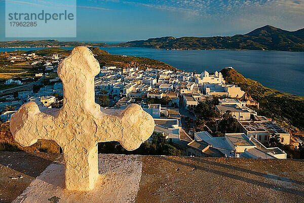 Griechisch-Orthodoxes Christentum Konzept Hintergrund  Fokus Blumen  christliche Kreuz mit Plaka Dorf auf Milos Insel im Hintergrund auf Sonnenuntergang  Plaka Stadt  Milos Insel  Griechenland  Europa