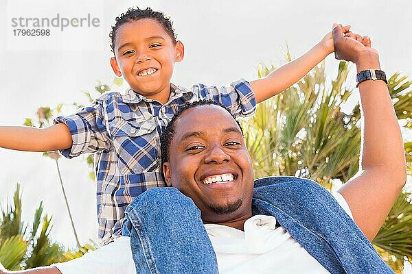 Glücklicher afroamerikanischer Vater und gemischtrassiger Sohn spielen im Park