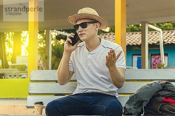 Ein attraktiver Mann  der mit einem Handy auf einer Bank telefoniert  ein Mann  der auf einer Bank sitzt und telefoniert