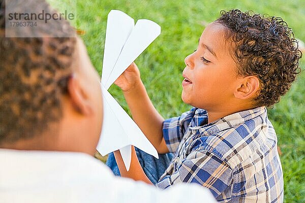 Glücklicher afroamerikanischer Vater und gemischtrassiger Sohn spielen mit Papierflugzeugen im Park