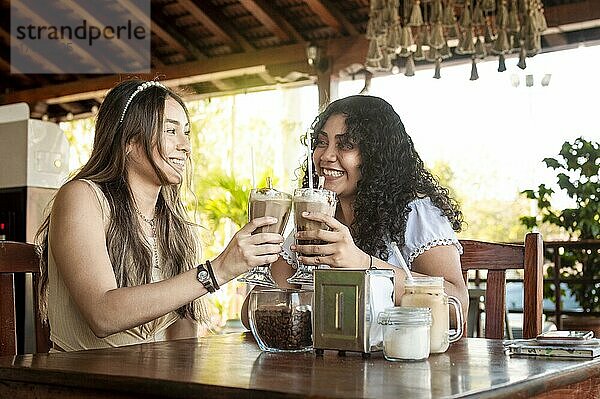 Zwei Mädchen trinken einen Milchshake  zwei Freundinnen in einem Café  zwei Mädchen prosten zu in einem Café an