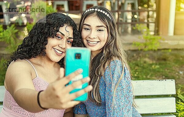 Zwei hübsche Mädchen sitzen auf einer Bank und machen ein Selfie  Mädchen lächeln und machen ein Selfie