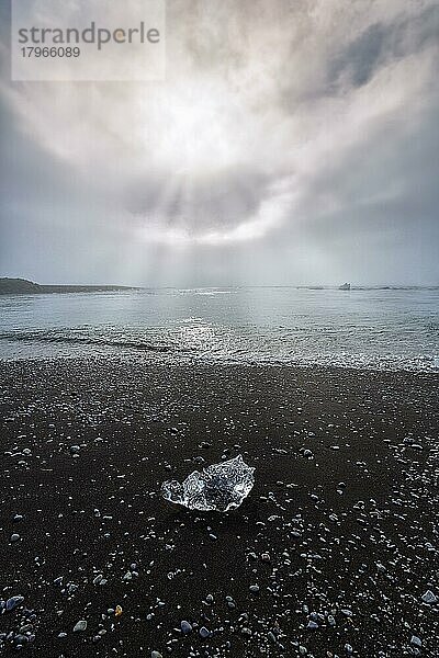 Eiskristall und Kieselsteine am schwarzen Lavastrand  von der Morgensonne angestrahlt  Gegenlicht  Sonnenstrahlen durch Dunst  Diamond Beach im Sommer  Jökulsárlón  Vatnajökull Nationalpark  Island  Europa