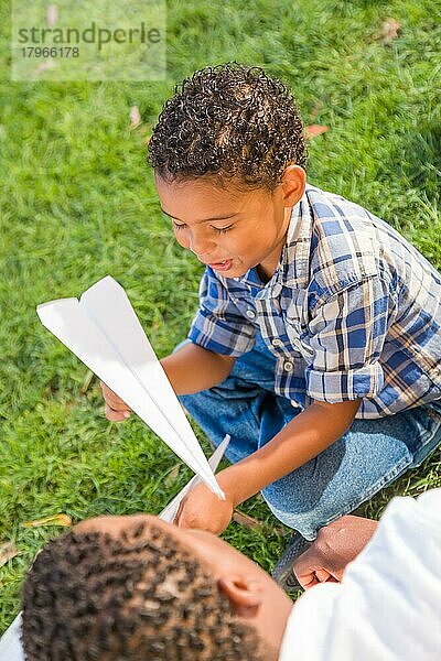 Glücklicher afroamerikanischer Vater und gemischtrassiger Sohn spielen mit Papierflugzeugen im Park