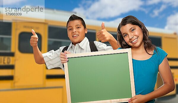 Junge hispanische Schüler mit leerer Kreidetafel in der Nähe des Schulbusses