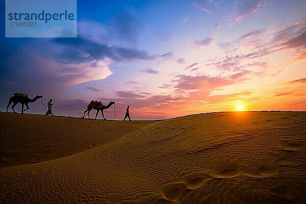 Indische Kameleers (Kameltreiber) Beduinen mit Kamel Silhouetten in Sanddünen der Wüste Thar bei Sonnenuntergang. Karawane in Rajasthan Reise Tourismus Hintergrund Safari Abenteuer. Jaisalmer  Rajasthan  Indien  Asien