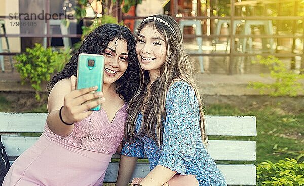 Zwei hübsche Mädchen sitzen auf einer Bank und machen ein Selfie  Mädchen lächeln und machen ein Selfie