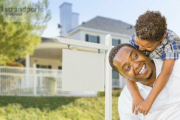 Glücklicher afroamerikanischer Vater und gemischtrassiger Sohn vor einem leeren Immobilienschild und einem neuen Haus