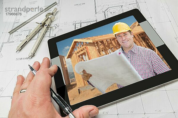 Hand eines Architekten auf einem Computertablett  der einen Bauunternehmer und ein Foto von einem Hausrahmen über Hausplänen  Zirkel und Lineal zeigt