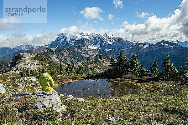 Wanderer sitzt auf einem Stein  Kleiner Bergsee am Tabletop Mountain  Mt. Shuksan mit Schnee und Gletscher  Mt. Baker-Snoqualmie National Forest  Washington  USA  Nordamerika