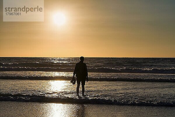 Mann  Silhouette  steht am Strand  im Wasser  Schuhe in der Hand  schaut auf das Meer  Sonnenuntergang  Atlantik  Frankreich  Europa