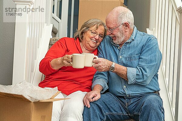 Müdes älteres erwachsenes Paar  das sich mit einer Tasse Kaffee auf der Treppe ausruht  umgeben von Umzugskartons