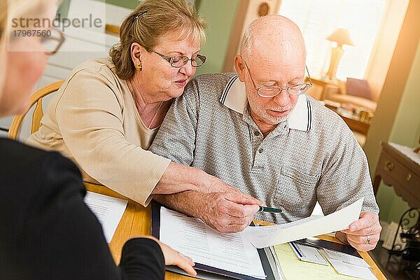 Älteres erwachsenes Paar  das mit einem Agenten bei der Unterzeichnung Dokumente in ihrer Wohnung durchgeht