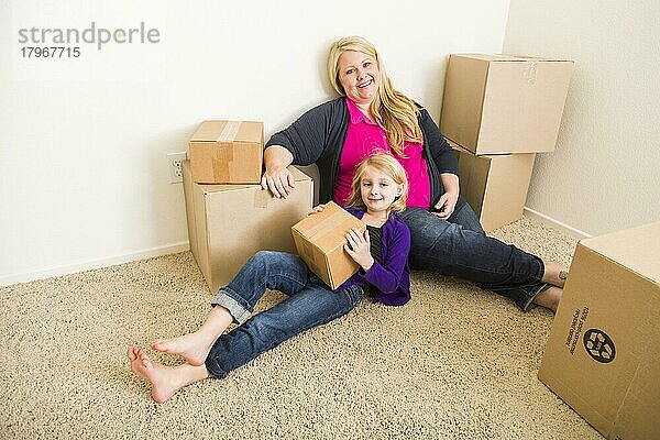 Glückliche junge Mutter und Tochter in einem leeren Raum mit Umzugskartons