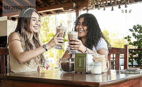 Zwei Mädchen trinken einen Milchshake  zwei Freundinnen in einem Café  zwei Mädchen prosten zu in einem Café an