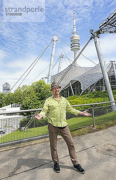 Freundlich lächelnder Mann beim Olympiaturm mit Olympia-Zeltdach  links BMW-Turm  Olympiapark  Olympiagelände  München  Oberbayern  Bayern  Deutschland  Europa
