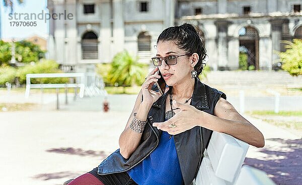Urban style girl sitting on a bench calling on the phone  An attractive girl sitting talking on the cell phone  Girl sitting in a park calling on the phone