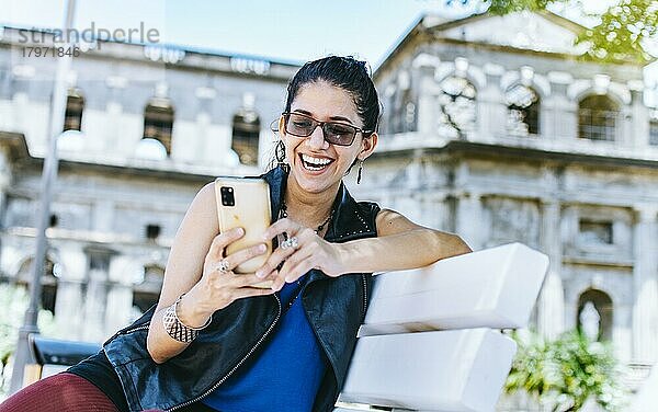 Ein attraktives Mädchen sitzt auf dem Handy lächelnd  Girl sitting on a bench texting on her cell phone  Urban style girl sitting on a bench with her cell phone