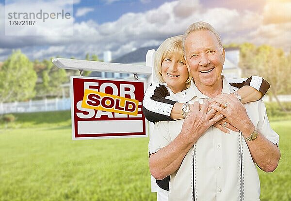Glückliches  liebevolles  älteres Paar  das sich vor einem verkauften Immobilienschild und Haus umarmt