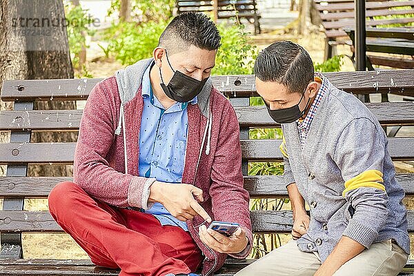 Zwei maskierte Männer überprüfen ihre Handys auf einer Bank  ein Mann zeigt einem anderen sein Handy